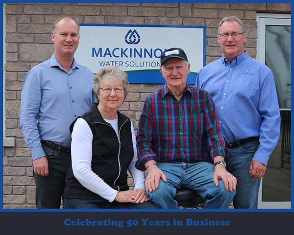 A smiling family poses proudly beside a well water tank in Sudbury, featuring the MacKinnon Water Solutions logo and celebrating 50 years of trusted service.
